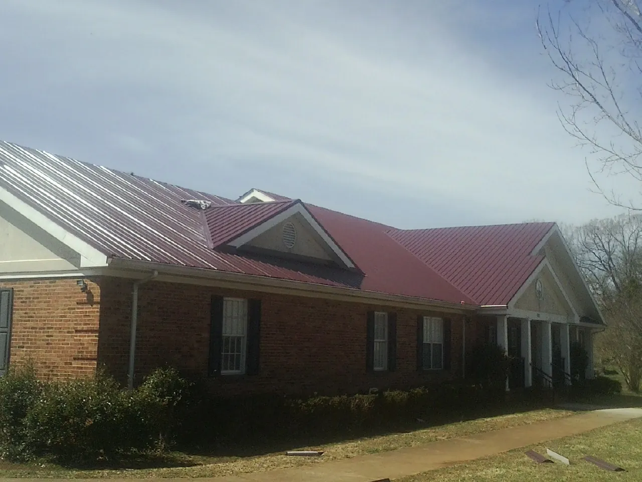 Red metal roof with gabled entries on a long brick building, from a Hail Damage Roof Repair job in Attica