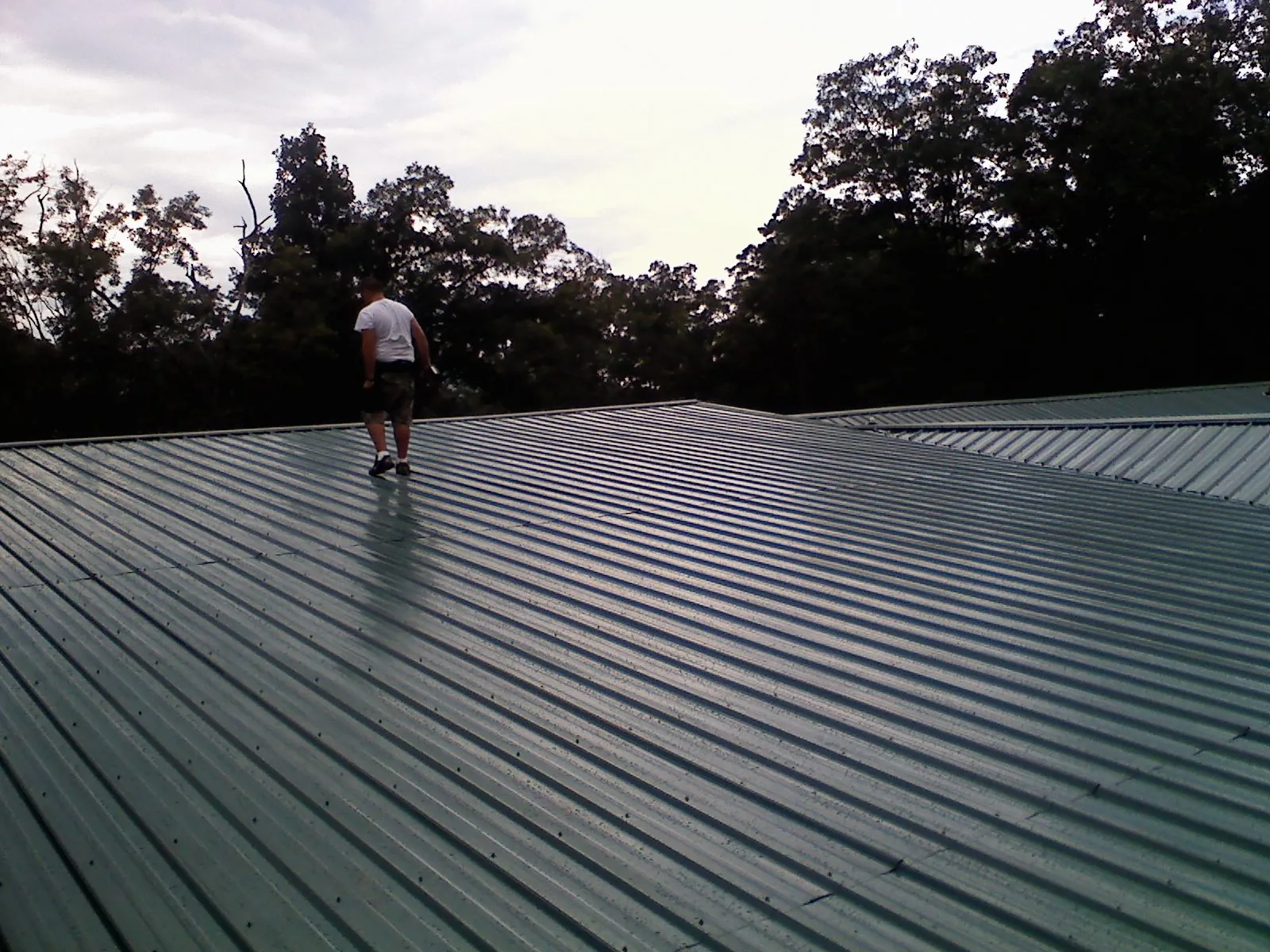 Roofer walking a wide expanse of new green metal roofing in Attica