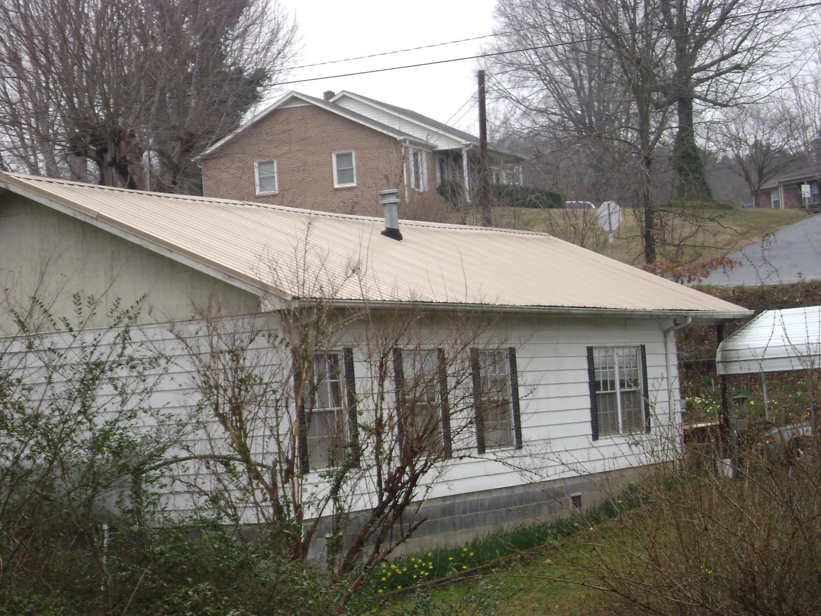 Tan metal roof on a white sided house set into a hillside — Commercial Roofing by Roofing Brothers in Attica