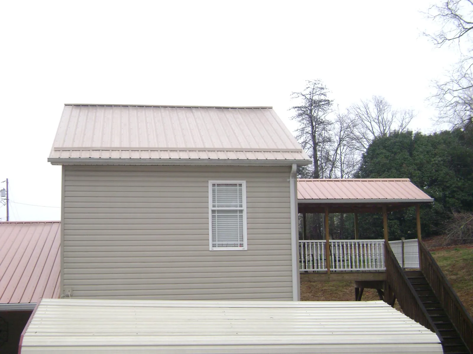 Tan metal roofs on a two story addition and attached porch, from a Roof Replacement job in Attica